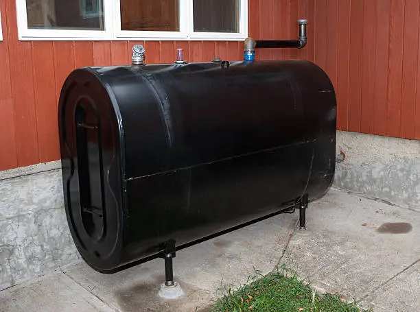 Black outdoor oil tank beside red building.